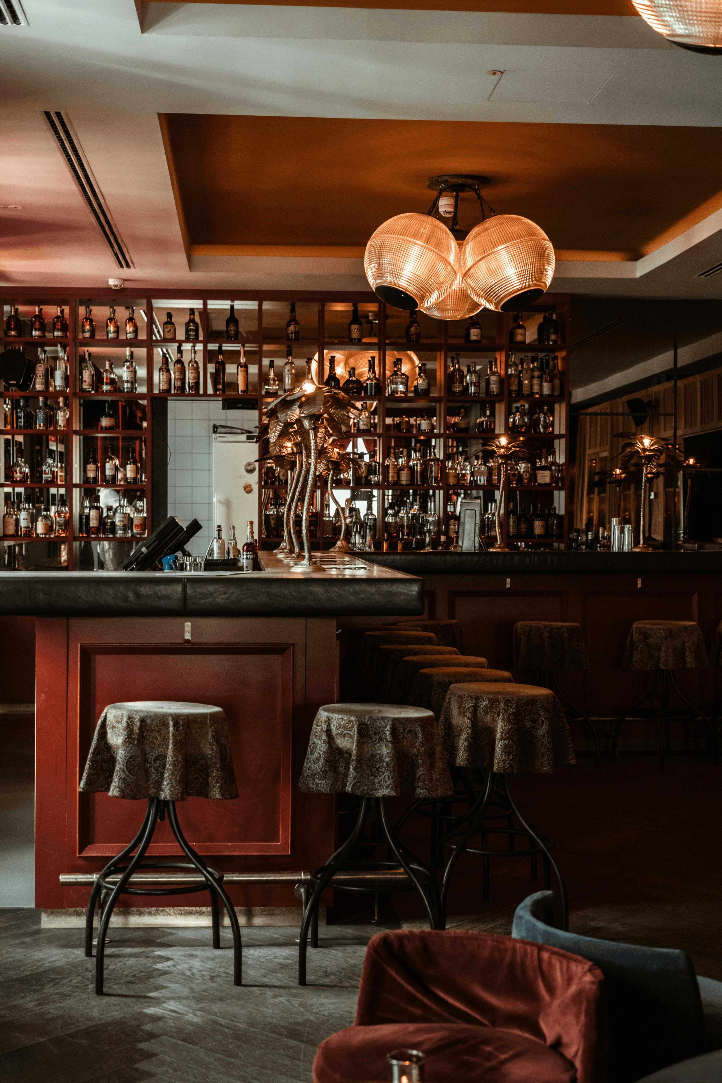 Picture of a bar, surrounded by stools. Coasy atmosphere and a display of bottles with various alcoholic drinks.